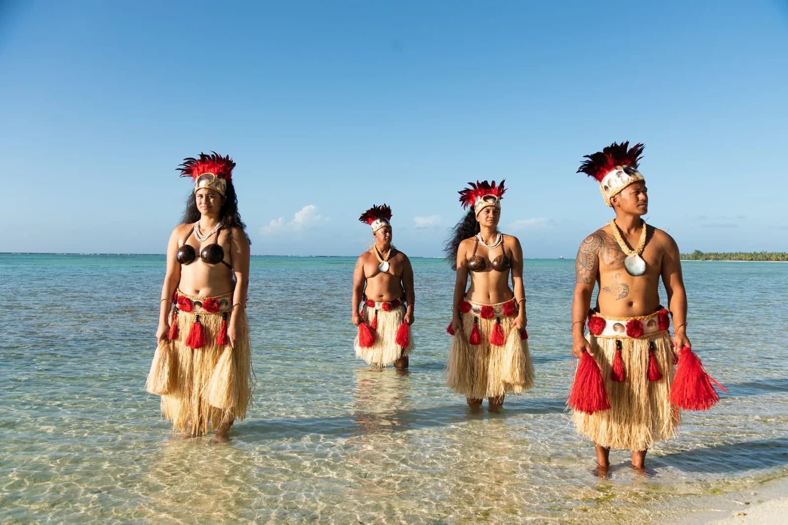 Four dancers in traditional dress standing in the shallow lagoon