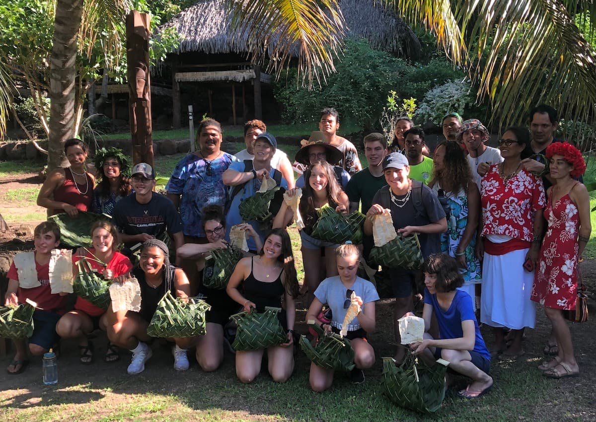 A large group of students and Polynesian teachers holding woven palm baskets
